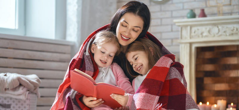 mom with kids under blanket with book
