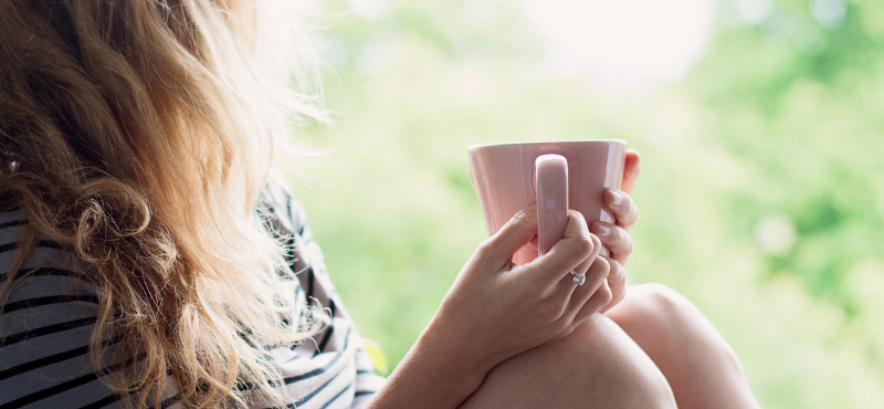 woman looking out the window while holding a pink mug