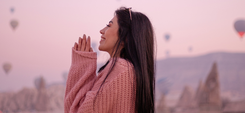 woman side view in pink sweater, looking happy. there's hot air balloons in the background