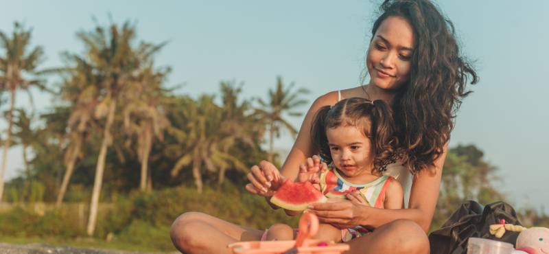 Mom and daughter eating a watermelon on a beach